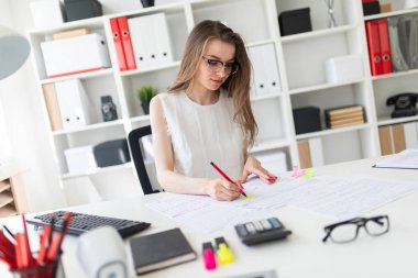Güzel genç kız ofiste masada oturmuş, elinde kalem tutan ve belgeleri doldurma.