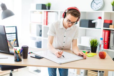 Gözlüklü ve kulaklıklı genç bir adam manyetik tahtaya bir işaret çizer..