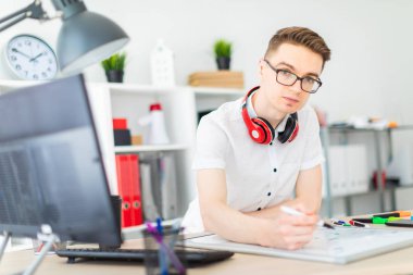 Gözlüklü genç bir adam bir bilgisayar masası duruyor. Genç bir adam bir işaretleyici manyetik bir tahtaya çizer. Çocuklar kulaklık boynuna asmak.