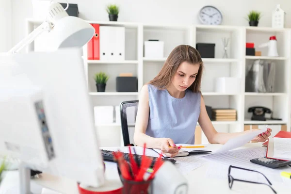 Hermosa joven en la oficina se sienta en una mesa y trabaja con un lápiz, bloc de notas y documentos . — Foto de Stock