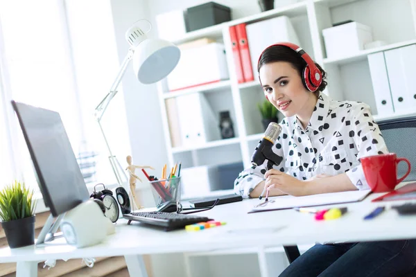 Güzel genç kız kulaklık bir mikrofon ofis masasında oturmuş. — Stok fotoğraf