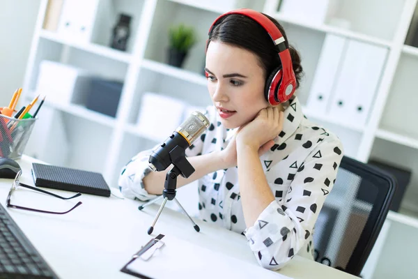 Krásná mladá dívka sedící v sluchátek a mikrofonem u stolu v kanceláři a mluví. — Stock fotografie