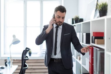 Adam rafları Ofisi yakınında duran, telefonda konuşurken ve üstünde belgili tanımlık ağıl elini koyarak.