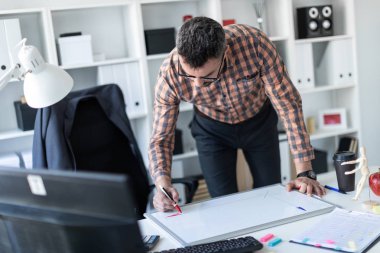 Bir adam ofiste masanın yanında duruyor ve bir işaretleyici manyetik tahtaya çizer.