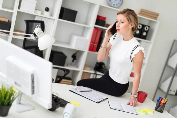 Молодая блондинка сидит за столом в офисе и разговаривает по телефону . — стоковое фото
