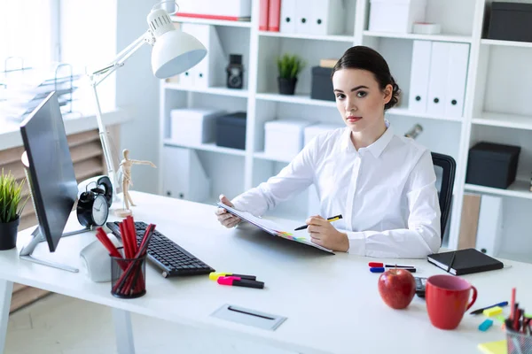 Een jong meisje zit in het kantoor, houdt een pen in haar hand en ziet er door middel van documenten. — Stockfoto