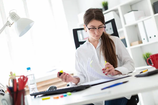 En ung flicka sitter vid ett bord på kontoret och håller texten i dokumentet med en gul markering. — Stockfoto