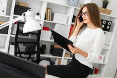 Genç kız ofiste, tabloda bir tablet sayfalarıyla birlikte onun elinde tutan ve telefonda konuşurken oturdu.