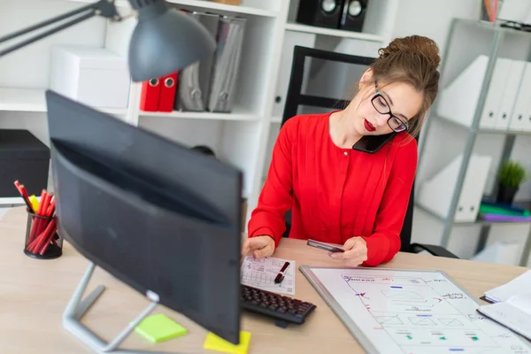 Een jong meisje zit bij het Bureau in het kantoor, bedrijf van een bankkaart in haar hand, het toetsenbord en praten over de telefoon. — Stockfoto