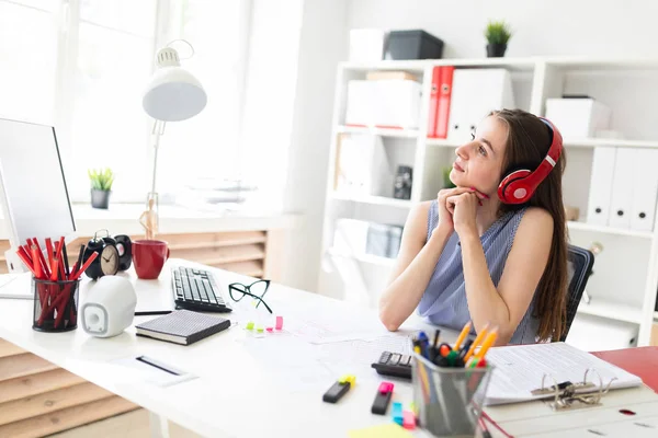 Güzel genç kız ofiste kırmızı kulaklıklar bir masada oturur.