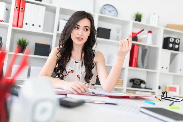 Güzel bir genç kız onun elinde belgeler ve bir kalem ile office masada oturuyor ve müzakere.