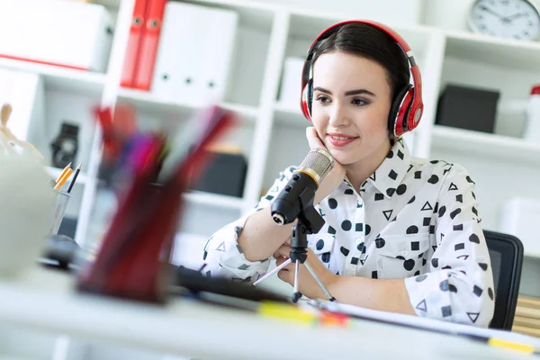 Belle jeune fille assise dans des écouteurs et avec microphone à table au bureau et parlant . — Photo