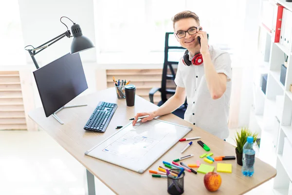 Gözlüklü genç bir adam bir bilgisayar masası duruyor ve telefonda konuşuyor. Önce onu bir manyetik kurulu ve işaretleri yatıyor. Çocuklar kulaklık boynuna asmak.