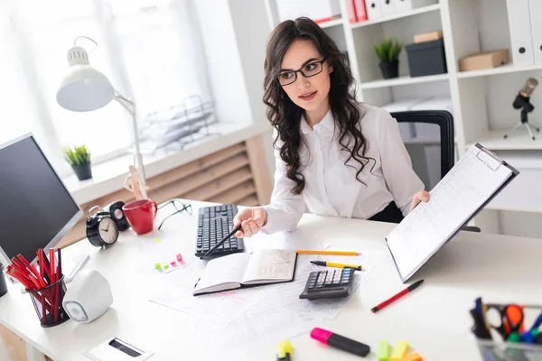 Een mooi jong meisje is zittend aan een tafel in het kantoor en een potlood wijzend op de informatie in het document. — Stockfoto