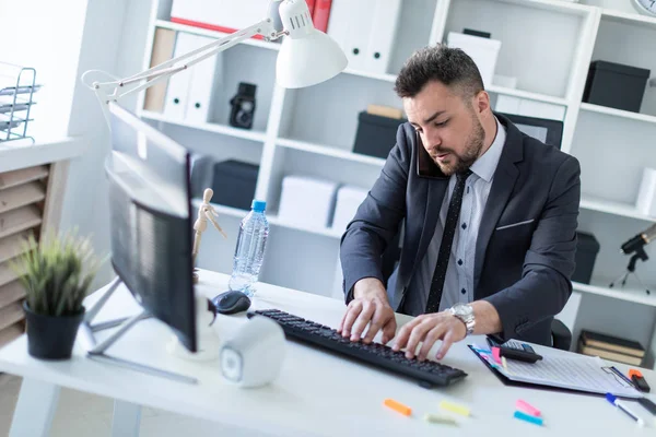 Bir adam masada ofiste oturur, onun omuz ile belgili tanımlık telefon çekmek ve klavyede yazdırır.