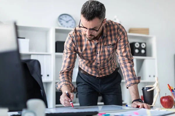 Bir adam ofiste masanın yanında duruyor ve bir işaretleyici manyetik tahtaya çizer.