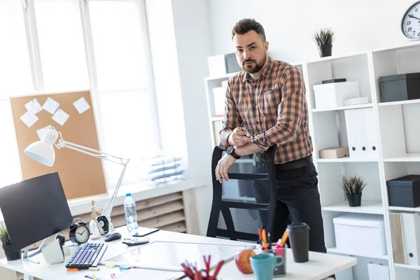 Bir adam bilgisayar masası yakınındaki ofiste standları ve sandalyenin arkasında ellerini koyar.