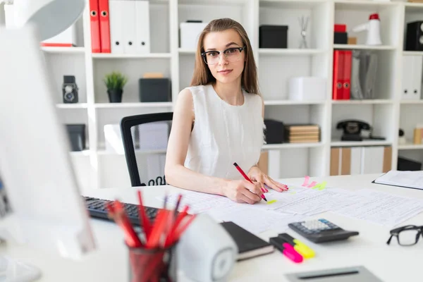 Mooi jong meisje zitten aan de tafel in het kantoor, houdt een pen in haar hand en invullen van de documenten. — Stockfoto