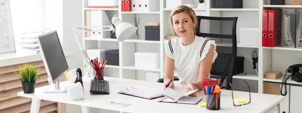 Een jong blond meisje zit achter een computerbureau in het kantoor, houdt een potlood in haar hand en werken met documenten. — Stockfoto