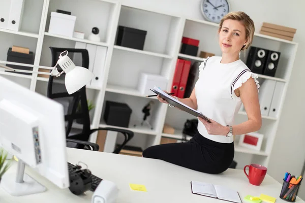 Una joven rubia está sentada en el escritorio de la oficina y tiene documentos y un lápiz.. — Foto de Stock