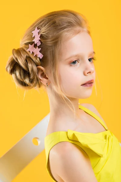 A girl is sitting on a white chair on a yellow background. — Stock Photo, Image