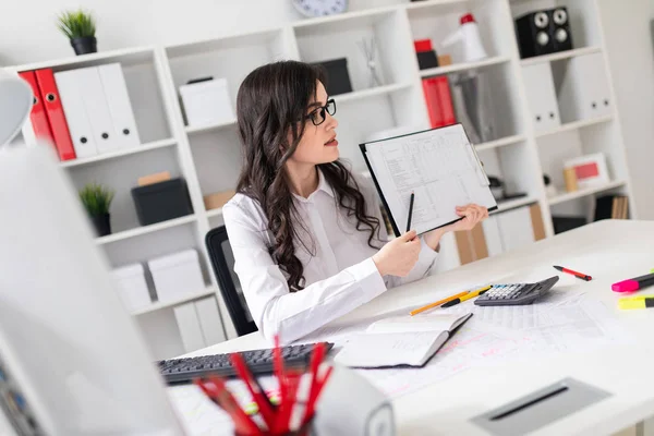 En vacker ung flicka sitter vid ett bord på kontoret och pekar en penna på information i dokumentet. — Stockfoto