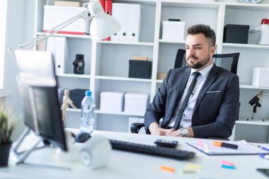 Bir adam masada ofiste bir sandalyede oturur ve ekrana görünüyor.