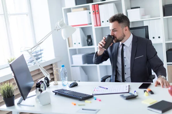 Bir adam masada ofiste oturur, kahve içer ve ekrana görünüyor.