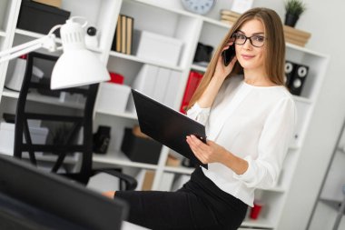 Genç kız ofiste, tabloda bir tablet sayfalarıyla birlikte onun elinde tutan ve telefonda konuşurken oturdu.