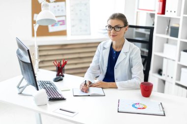 Beyaz bir elbise içinde genç bir kız ofiste masalarda oturur ve bir kalem elinde tutar. Bir stetoskop boynunda asılı.