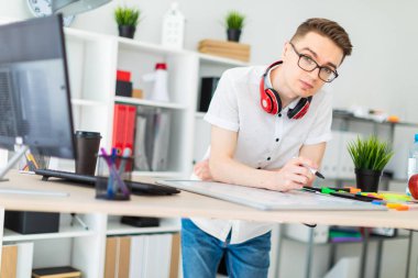 Gözlüklü genç bir adam bir bilgisayar masası duruyor. Genç bir adam bir işaretleyici manyetik bir tahtaya çizer. Çocuklar kulaklık boynuna asmak.