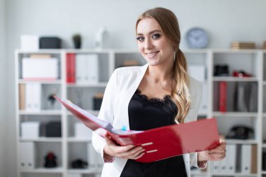 Genç bir kız ofis raf yanında duruyor ve bir klasör belgeler ile onun elinde tutan.