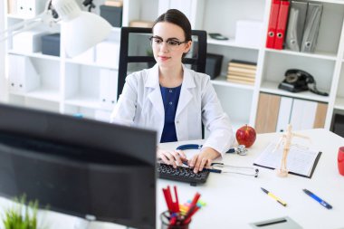 Beyaz bir elbise içinde güzel bir genç kız masada oturan ve klavyede yazarak.