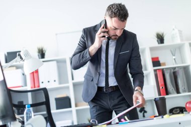 Bir adam ofiste bir tabloda yakın duran, telefonda konuşurken ve belgeler üzerinden çevirme.