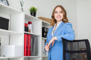 Güzel bir genç kız ofiste, bir raf yakınındaki bir dirsek bir sandalyenin arkasına koyarak standları.