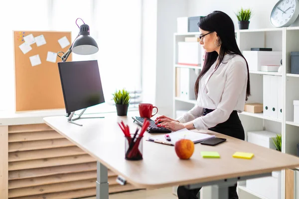 Genç bir kız masanın ayakta ve metin klavyede yazarak. Belgeler ve bir işaretleyici kızın yanında yalan.