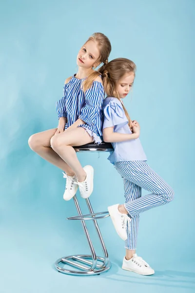 Kızlar ikizler mavi elbise bir barın yakınında poz ışık mavi bir arka plan üzerinde tabure.