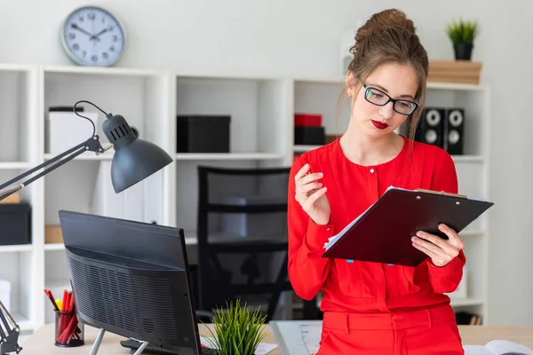 Genç bir kız bir masaya eğilmiş duruyor ve bir kalem ve belgeleri düzenliyor.