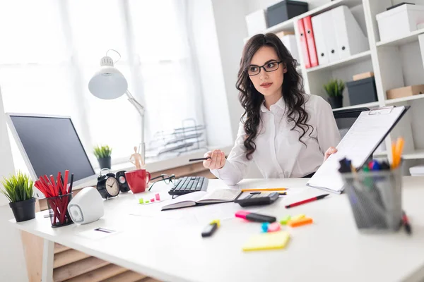 Una hermosa jovencita está sentada en una mesa en la oficina y señalando con un lápiz la información del documento . — Foto de Stock