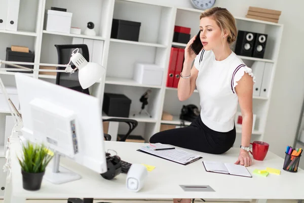 Молодая блондинка сидит за столом в офисе и разговаривает по телефону . — стоковое фото
