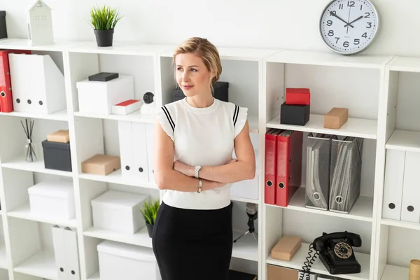 Genç sarışın kız Office belgeleri ile bir raf yanında duruyor.
