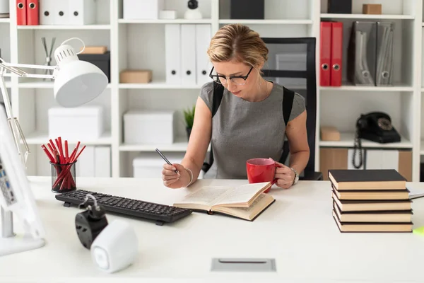 Ofisteki bir masada oturan genç bir kız elinde bir kalem ve kırmızı bir bardak tutuyor. Kız açık bir kitap gibi yalan söylemeden önce.