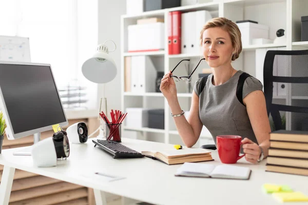 Genç bir kız ofiste bir masada oturuyor ve elinde kırmızı bir bardak ve gözlük tutuyor. Kız açık bir kitap gibi yalan söylemeden önce.
