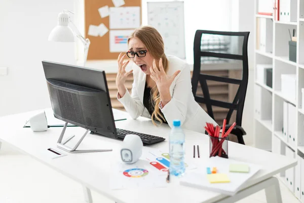 Una joven está sentada en una mesa de la oficina, mirando al monitor y doblando los dedos . — Foto de Stock