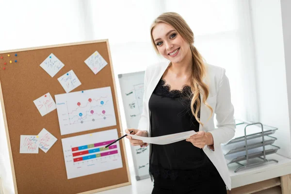 En ung flicka står nära en styrelse med klistermärken och innehar ett dokument och en penna i händerna. — Stockfoto