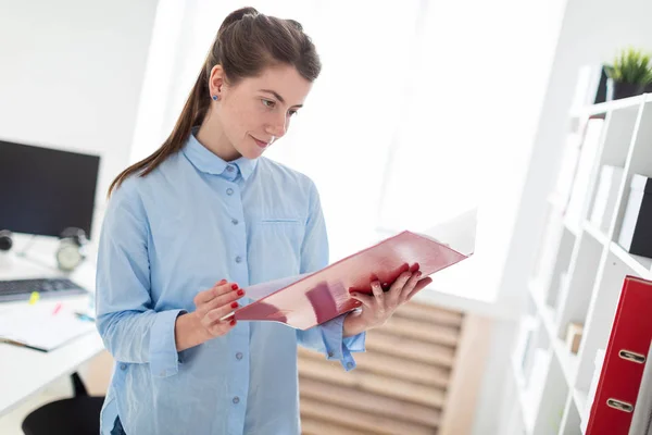 Молода дівчина в офісі стоїть біля притулку і прокручує через папку з документами . — стокове фото