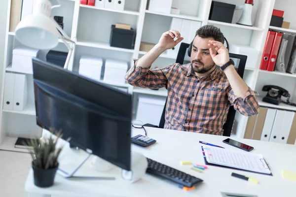 A young man in headphones sits at a table in the office and looks at the monitor. — Stock Photo, Image