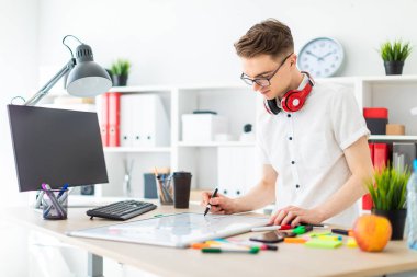Gözlüklü genç bir adam bir bilgisayar masası duruyor. Genç bir adam bir işaretleyici manyetik bir tahtaya çizer. Çocuklar kulaklık boynuna asmak.