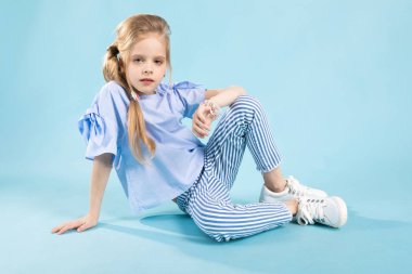 Mavi elbiseleri bir kız mavi bir arka plan üzerinde oturuyor.