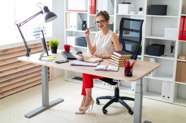 Genç bir kız bir bilgisayar masada oturur ve açık bir kitap ve bir kalem tutan eline.